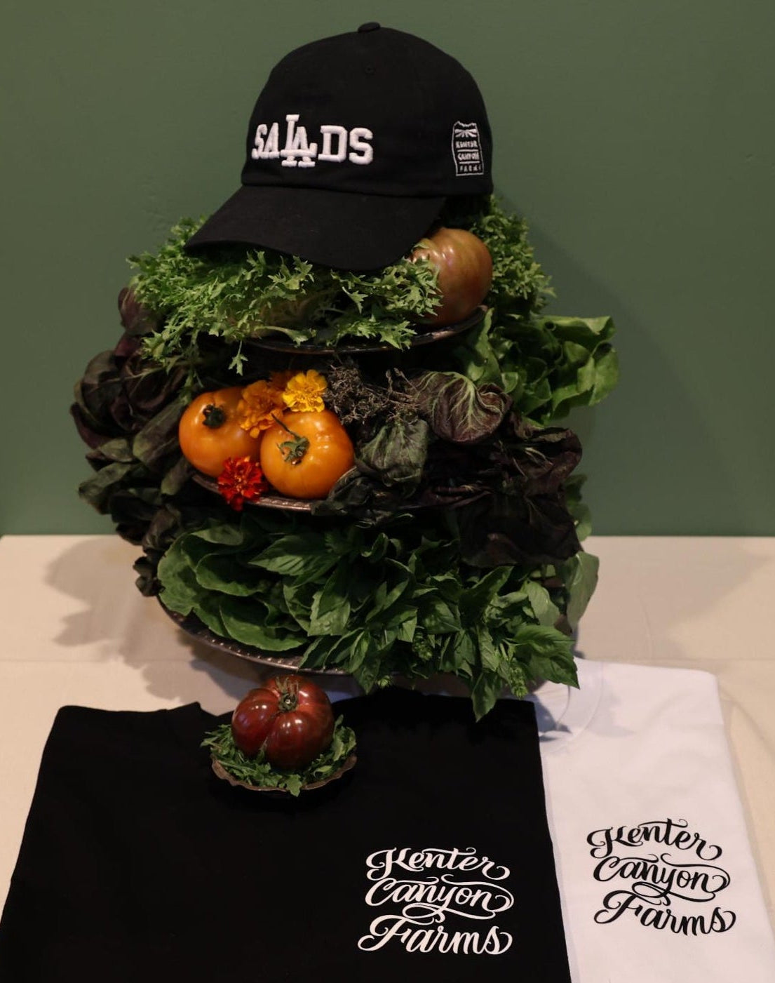 Decorative vegetable display with black hat on top. Black and white t-shirt on table.