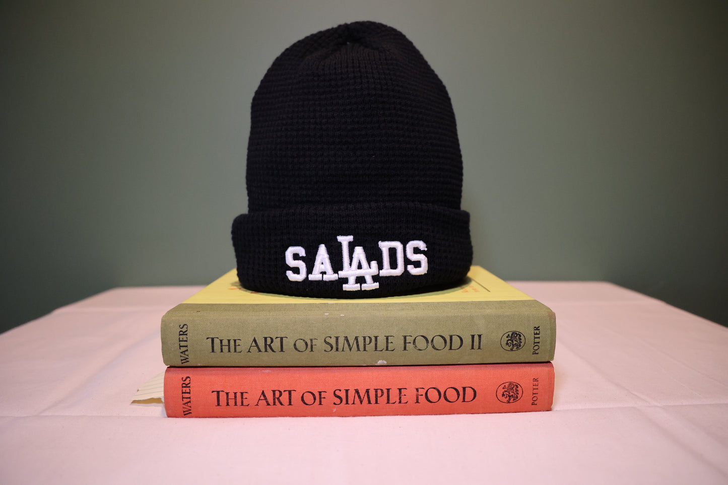 Black beanie with 'SALADS' on top of two books titled 'The Art of Simple Food.'