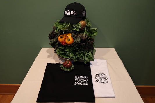 Decorative vegetable display with black hat on top. Black and white t-shirt on table.