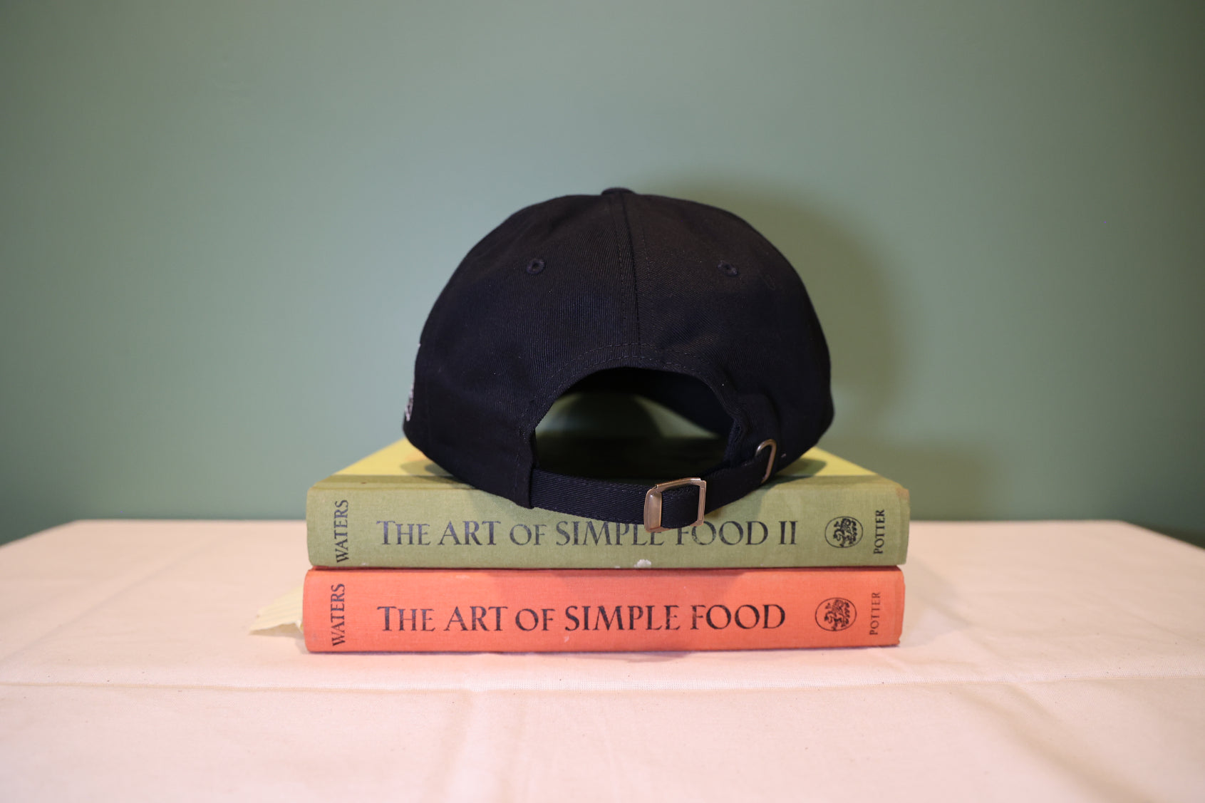 Black cap on top of two books titled 'The Art of Simple Food' with a plain background