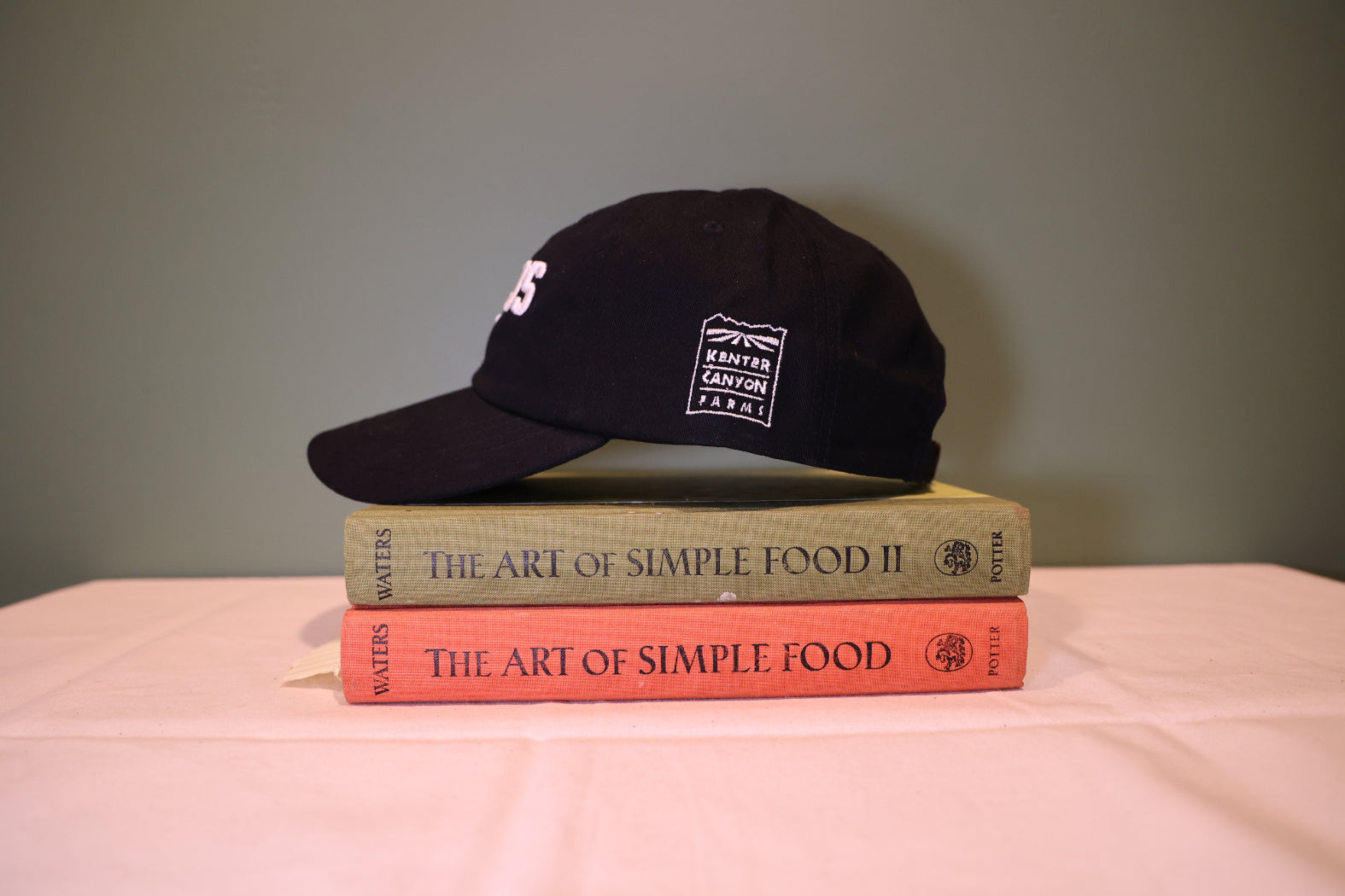 Black cap on top of two books titled 'The Art of Simple Food' with a plain background