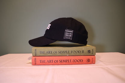 Black cap on top of two books titled 'The Art of Simple Food' with a plain background